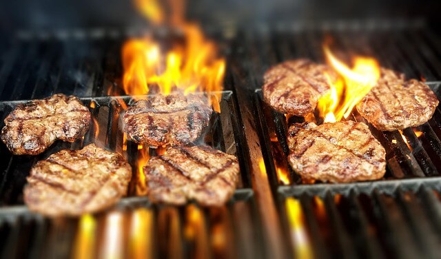 Burgers with grill marks cooking over flames on a hot grill, illustrating high-heat cooking.